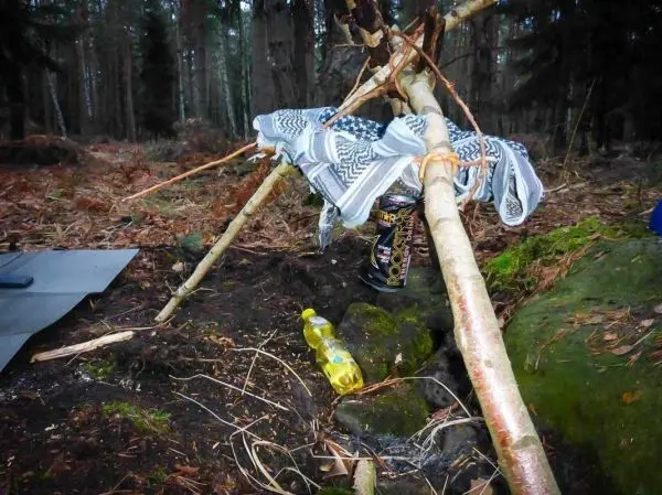 Improvisierte Tarp-Notunterkunft aus Ästen und Tuch über einem Stein