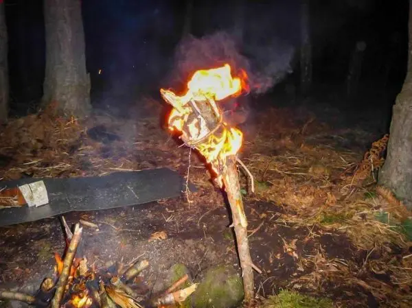 Kleine Flamme brennt an einem Holzstock über einem Bodenfeuer