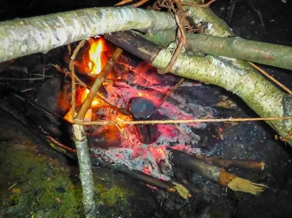 Kleine Flamme brennt zwischen Holzstücken auf glühenden Kohlen