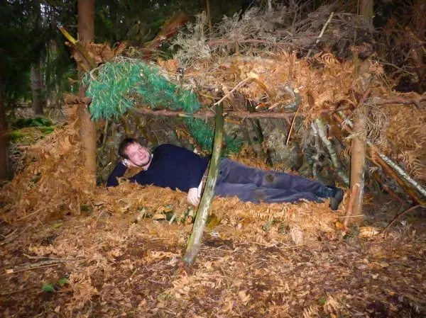 Person liegt in einem selbstgebauten Unterschlupf aus Ästen und Blättern