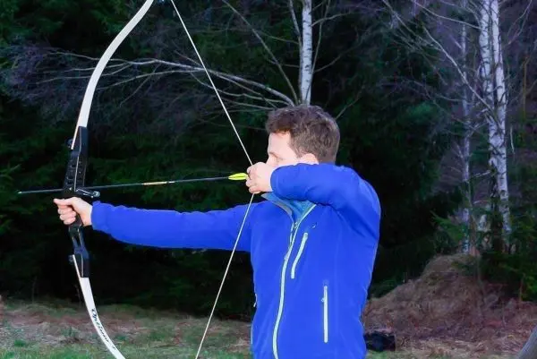 Bogen wird gespannt, Pfeil zielt auf ein Ziel im Wald