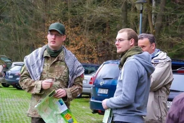 Drei Personen betrachten eine Karte auf einem Parkplatz zwischen Autos