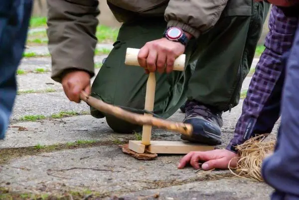 Feuerbohrer wird mit einem Stock auf einen Zunderblock gedrückt