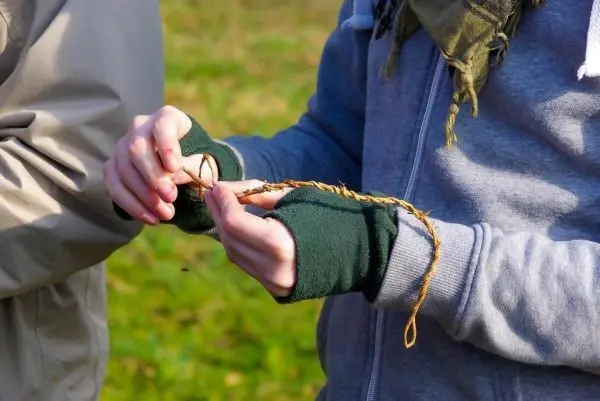 Hände flechten eine Schnur aus Pflanzenmaterial