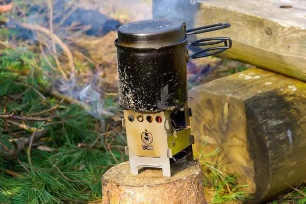 Hobo-Kocher mit Kessel auf Baumstamm, Dampf steigt auf