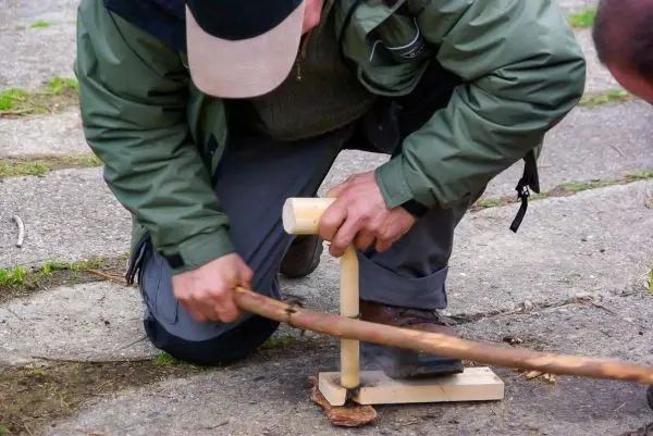 Holzstück wird mit einem Stock bearbeitet, um Glut zu erzeugen
