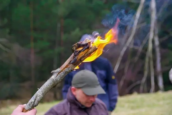 Kleine Flamme brennt an einem Stock, Rauch steigt auf