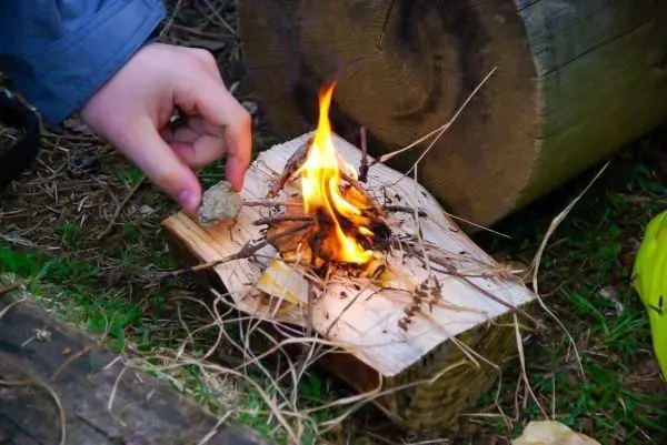 Kleine Flamme brennt auf einem Holzstück mit Zunder und Ästen