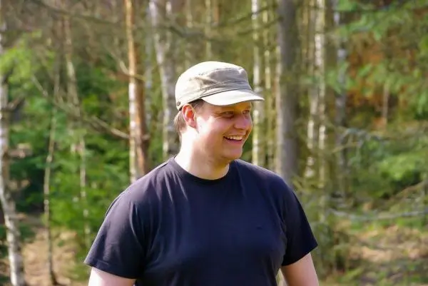 Lächelnde Person steht im Wald zwischen Bäumen