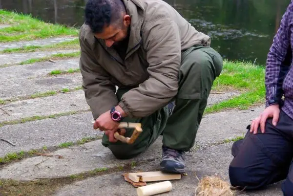 Mann bearbeitet Holzstück mit einem Messer auf dem Boden