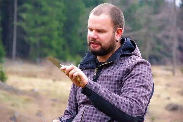 Mann hält ein Messer in der Hand und betrachtet die Klinge aufmerksam