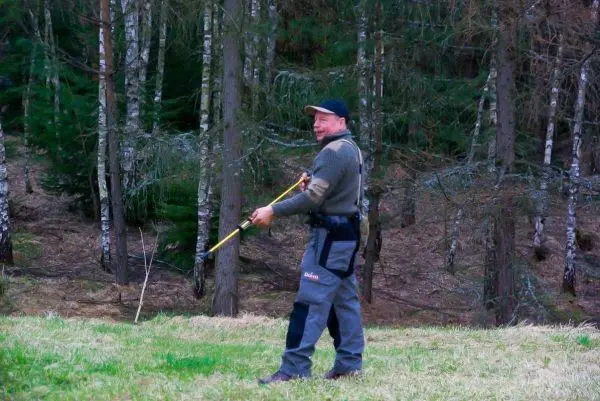 Mann hält einen Stock in der Hand und steht auf einer Wiese im Wald