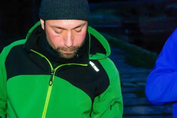 Mann in grüner Jacke betrachtet Boden, während es dunkel ist