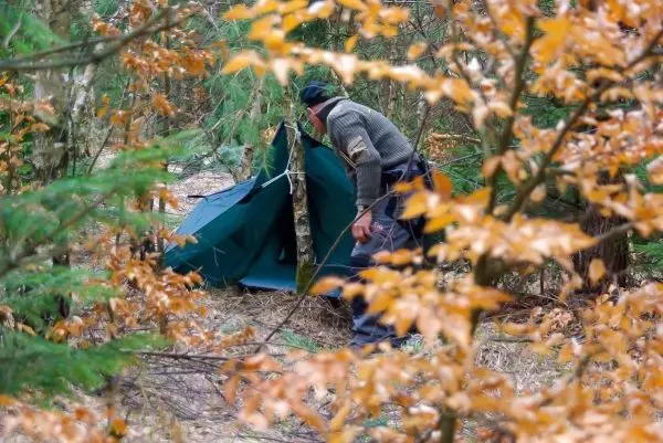 Mann richtet Tarp-Notunterkunft im Wald auf