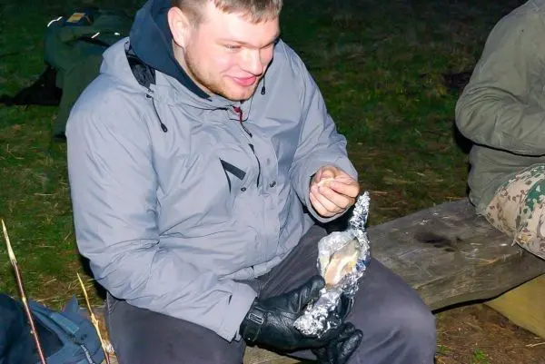 Mann sitzt an einem Tisch und hält in Alufolie eingewickelten Fisch