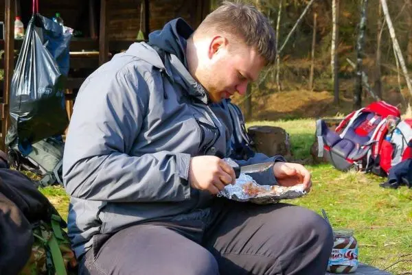 Mann sitzt auf dem Boden und isst aus Alufolie mit einem Messer