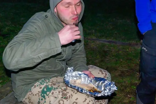 Mann sitzt auf dem Boden und isst aus einer Alufolie verpackten Fisch