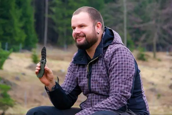 Mann sitzt im Freien und hält ein Klappmesser in der Hand
