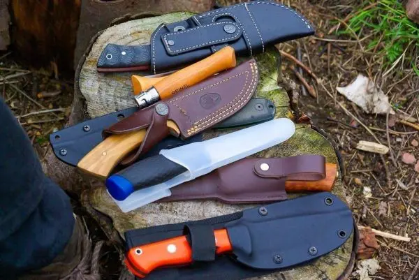 Mehrere Messer mit unterschiedlichen Klingen und Scheiden auf einem Baumstumpf angeordnet