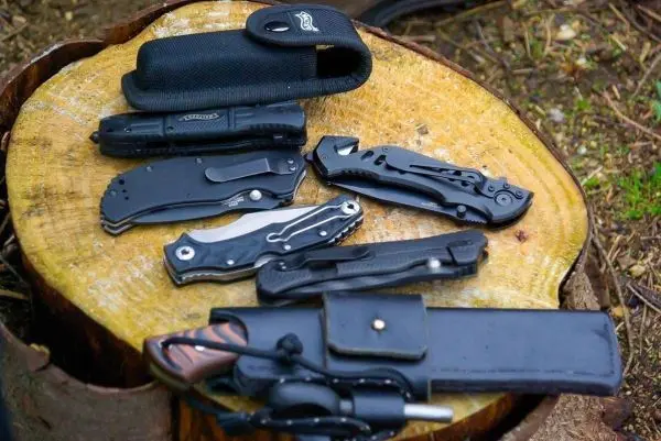 Mehrere Taschenmesser und ein Holster liegen auf einem Baumstumpf