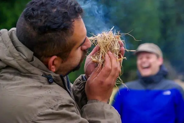 Person hält trockenes Gras und bläst darauf