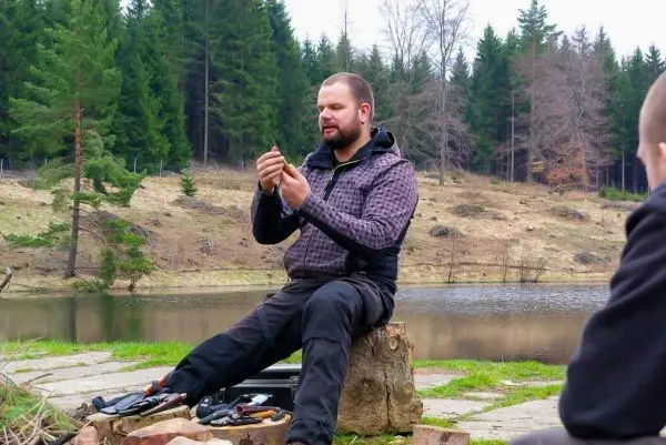 Person sitzt auf einem Baumstumpf und zeigt ein Werkzeug