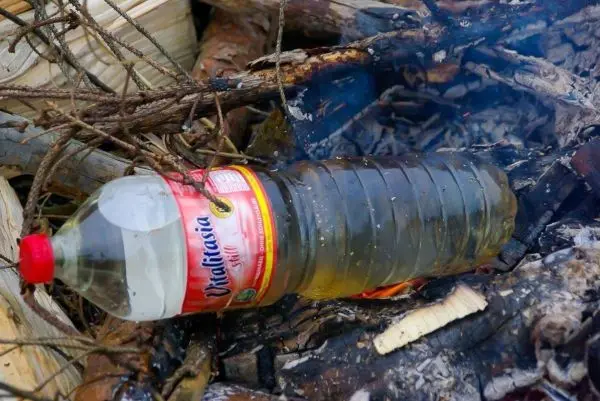 Plastikflasche mit Flüssigkeit liegt auf glühenden Holzstücken