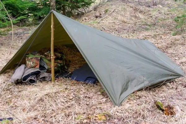 Tarp-Notunterkunft mit Holzstütze und Unterlage aus Laub und Kleidung