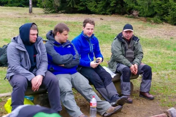 Vier Personen sitzen auf einer Holzbank in der Natur, umgeben von Bäumen