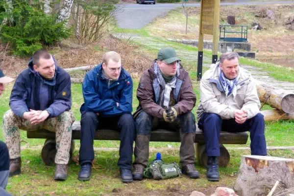 Vier Personen sitzen auf einer Holzbank in einer natürlichen Umgebung