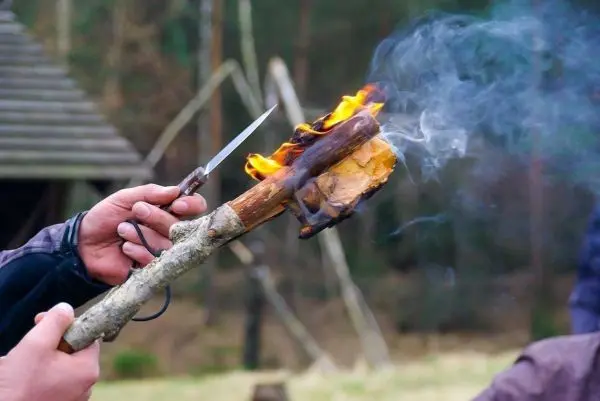 Zunder glimmt an einem Holzstück, während ein Messer gehalten wird