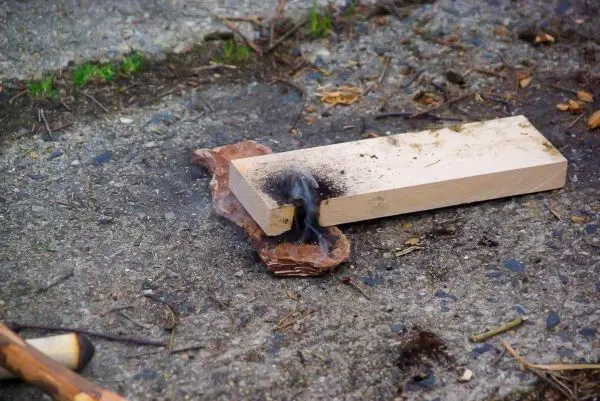 Zunder glimmt auf einer Holzplatte, Rauch steigt auf