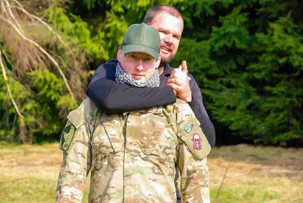 Zwei Personen in militärischer Kleidung, eine Person hält die andere von hinten fest