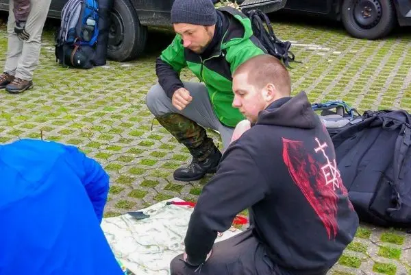 Zwei Personen knien um eine Karte auf dem Boden, Rucksäcke im Hintergrund