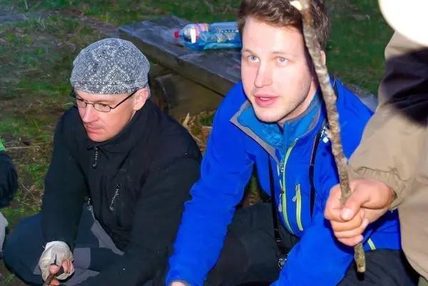 Zwei Personen sitzen auf dem Boden und halten Stöcke