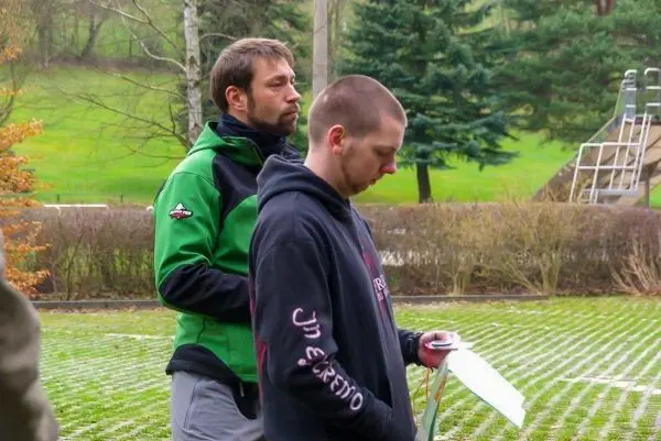 Zwei Personen stehen auf einer Wiese, eine hält ein Blatt Papier in der Hand