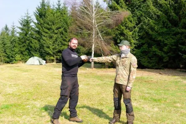 Zwei Personen stehen auf einer Wiese und führen eine Übergabe durch