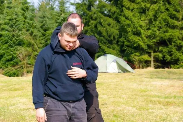 Zwei Personen üben eine Technik zur Kontrolle in einem Freigelände mit Zelt