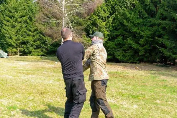 Zwei Personen üben eine Technik zur Kontrolle in einem offenen Gelände