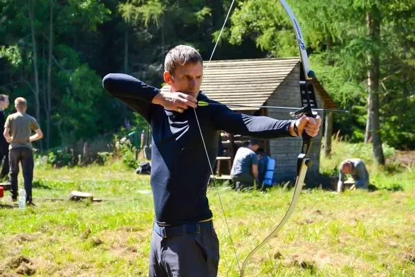 Bogen wird gespannt, Pfeil zielt auf ein Ziel im Hintergrund