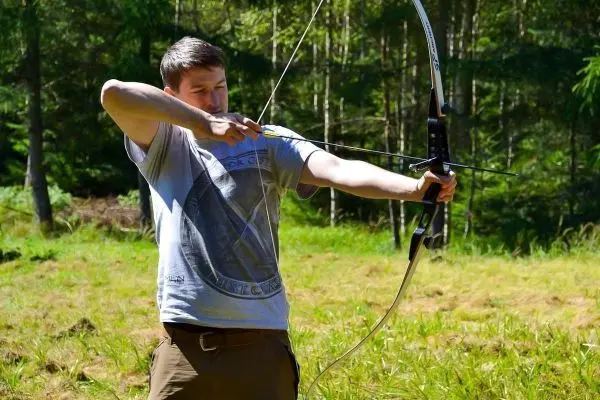 Bogen wird gespannt, Pfeil zielt auf ein Ziel im Wald