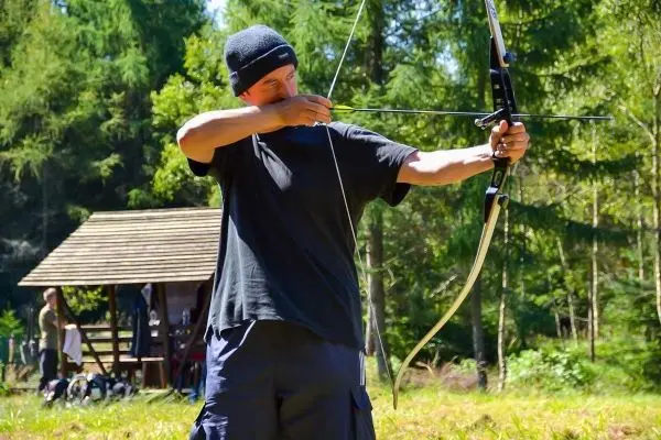 Bogenschütze spannt Pfeil in einem Waldgebiet