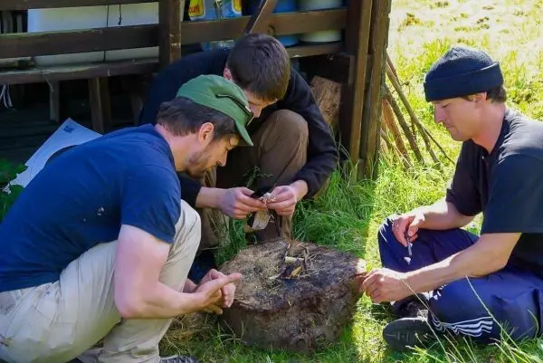Drei Personen arbeiten gemeinsam an einem Holzstamm beim Feuer machen