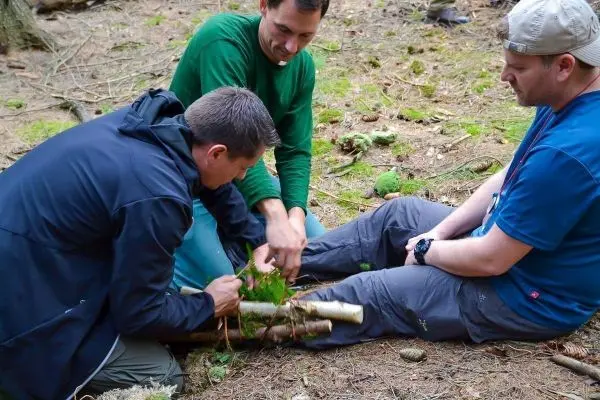 Drei Personen arbeiten gemeinsam an einer Holzstruktur im Wald