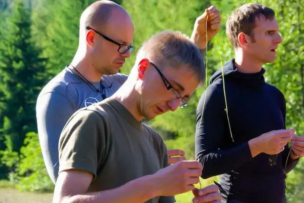 Drei Personen fädeln Schnüre durch kleine Ösen in der Natur
