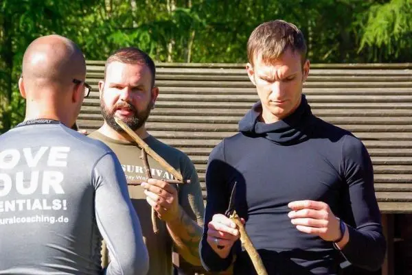 Drei Personen halten Holzstöcke und diskutieren Techniken im Freien