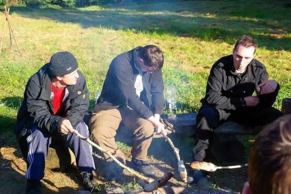 Drei Personen rösten Lebensmittel über einem offenen Feuer mit langen Stöcken