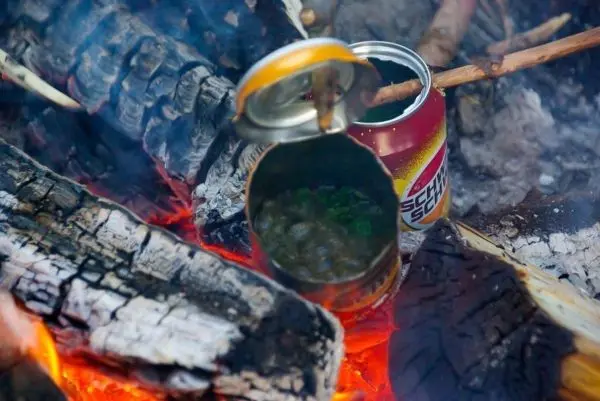 Eisenbehälter kocht über Glut zwischen Holzscheiten