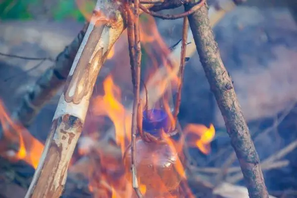 Flasche hängt über einem Feuer zwischen Ästen