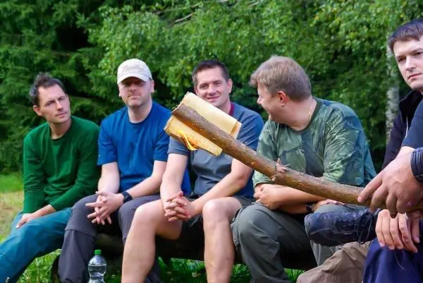 Fünf Personen sitzen auf einer Bank im Freien und beobachten einen Stock mit Rinde